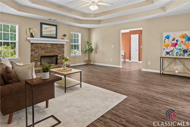living room with a raised ceiling, wood finished floors, a ceiling fan, baseboards, and plenty of natural light