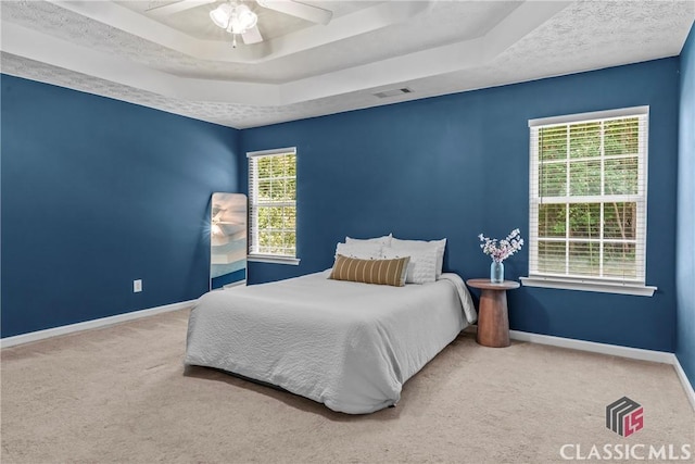 carpeted bedroom with baseboards, a raised ceiling, and a ceiling fan