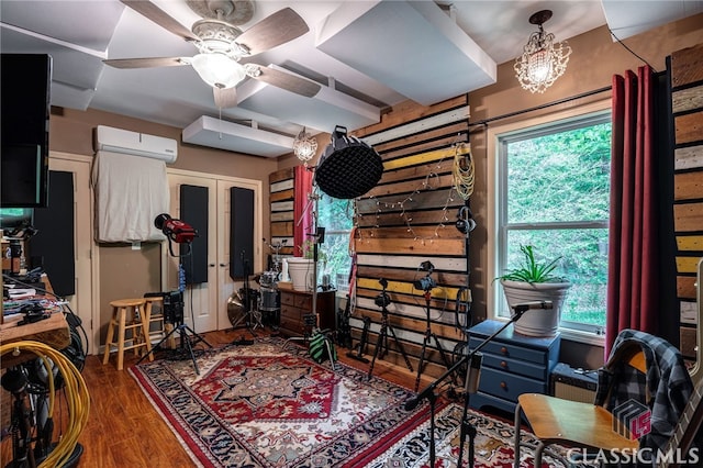 living room with a wall mounted AC, wood finished floors, ceiling fan, and healthy amount of natural light