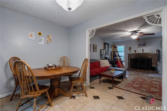 dining space with a textured ceiling, light tile patterned floors, a ceiling fan, a brick fireplace, and baseboards