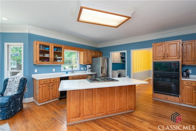 kitchen with black appliances, a sink, light countertops, light wood-type flooring, and glass insert cabinets