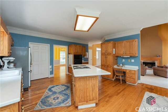kitchen featuring cooktop, light wood-style flooring, light countertops, ornamental molding, and a center island