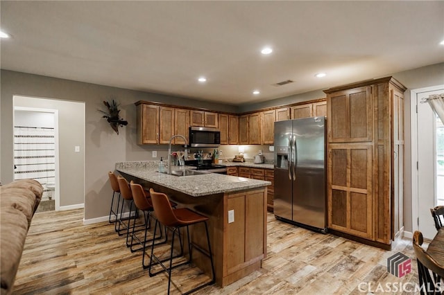 2100 New Hope Church Rd, Comer, GA 30629 - kitchen featuring appliances with stainless steel finishes, a peninsula, light wood-style floors, a breakfast bar, and brown cabinets