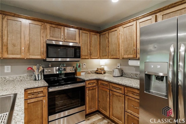 2100 New Hope Church Rd, Comer, GA 30629 - kitchen with stainless steel appliances, brown cabinets, light stone counters, and light wood-type flooring