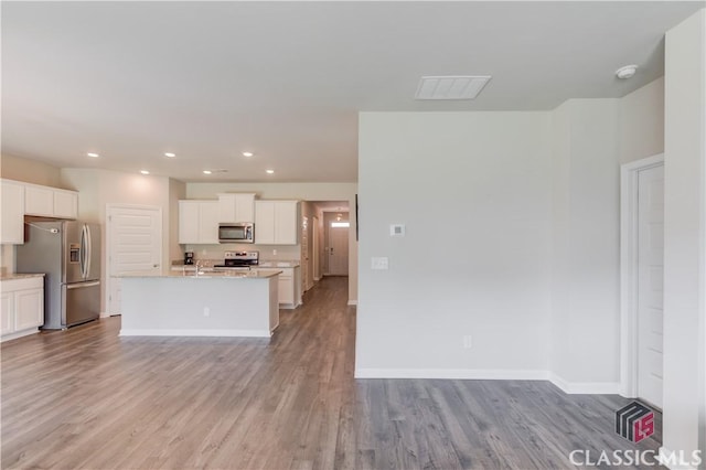 334 Pepin Ct, Hoschton, GA 30548 - kitchen featuring appliances with stainless steel finishes, wood finished floors, white cabinetry, a kitchen island with sink, and baseboards