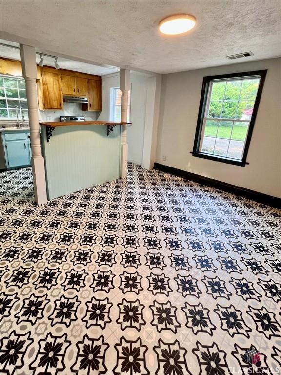 180 N Poplar St, Athens, GA 30601 - kitchen featuring under cabinet range hood, a textured ceiling, baseboards, a sink, and brown cabinets