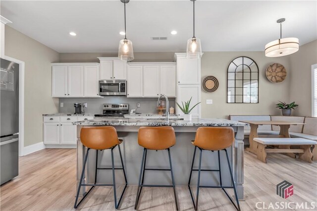 1810 Willow Creek Dr, Watkinsville, GA 30677 - kitchen with stainless steel appliances, a sink, a kitchen bar, white cabinets, and light wood finished floors