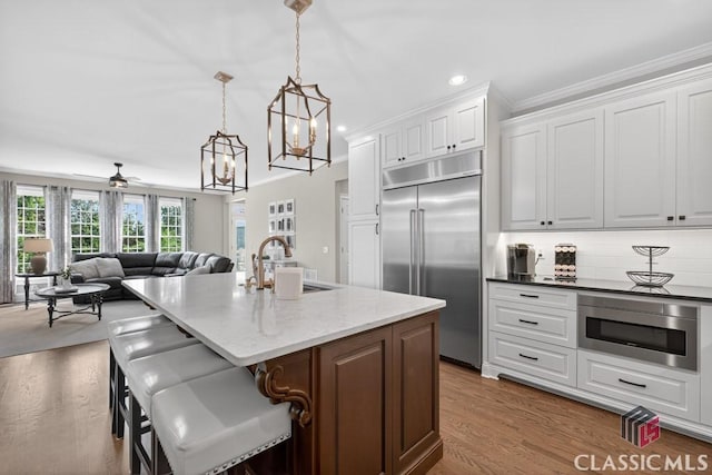 1232 Everton Pl, Cumming, GA 30041 - kitchen featuring built in appliances, crown molding, white cabinetry, backsplash, and a center island with sink