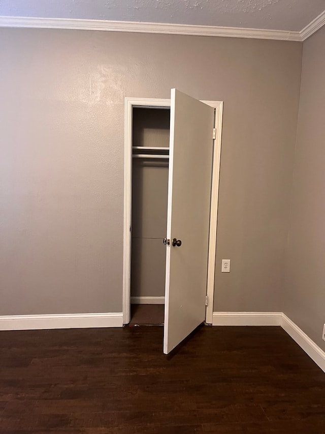 unfurnished bedroom with a closet, baseboards, wood finished floors, and crown molding