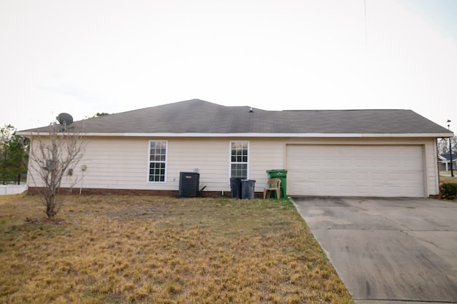 rear view of property featuring driveway, a garage, central AC unit, and a lawn