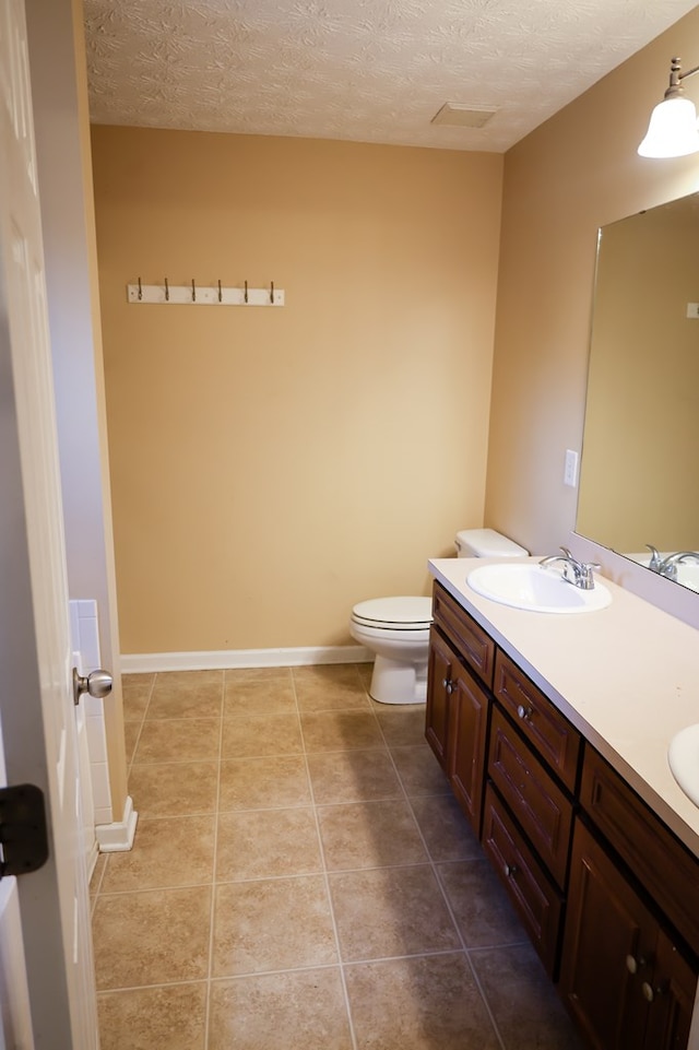 bathroom with a textured ceiling, tile patterned flooring, toilet, a sink, and double vanity