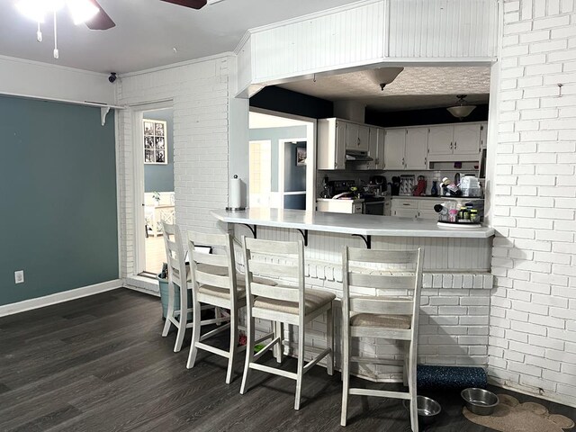 kitchen featuring dark wood-style floors, under cabinet range hood, electric range, and brick wall