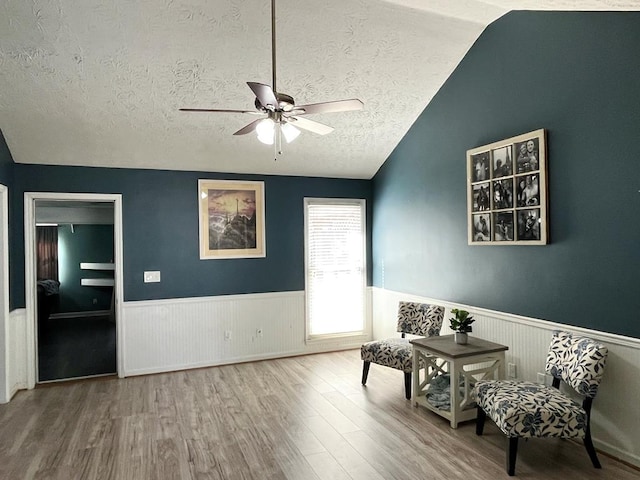 unfurnished room with a wainscoted wall, lofted ceiling, ceiling fan, a textured ceiling, and wood finished floors