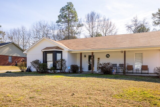 single story home featuring brick siding, a shingled roof, covered porch, and a front yard