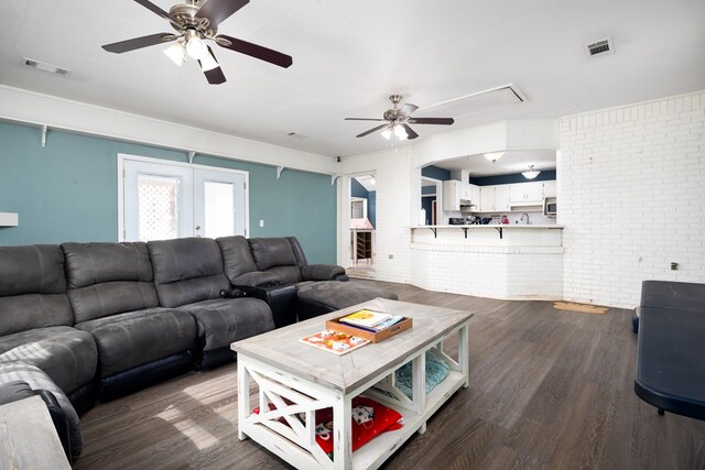 living area featuring brick wall, dark wood-type flooring, visible vents, and attic access