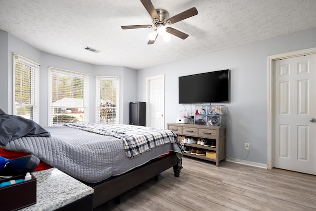 bedroom featuring light wood-style floors, visible vents, a textured ceiling, and baseboards