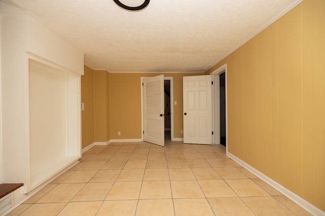 tiled empty room featuring a textured ceiling, ornamental molding, and wood walls