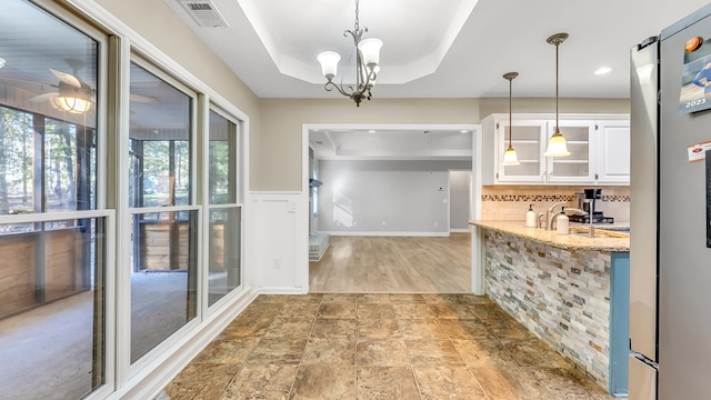 kitchen featuring a raised ceiling, light stone counters, white cabinets, and pendant lighting