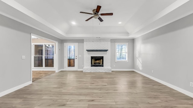 unfurnished living room with ceiling fan, a raised ceiling, light wood-type flooring, and a brick fireplace