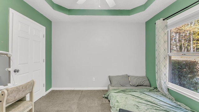 bedroom featuring ceiling fan, light colored carpet, and a tray ceiling