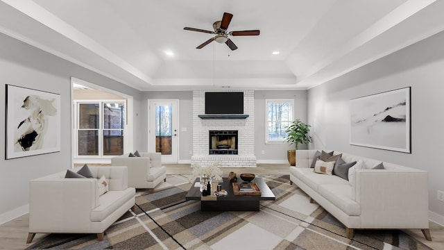 living room featuring hardwood / wood-style floors, ceiling fan, a fireplace, and a tray ceiling