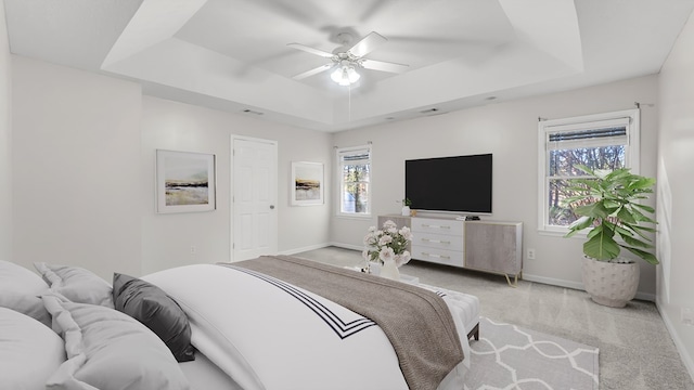 bedroom featuring a tray ceiling, multiple windows, light colored carpet, and ceiling fan