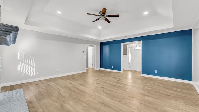 spare room featuring light wood-type flooring, a tray ceiling, and ceiling fan