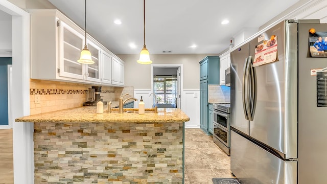 kitchen featuring kitchen peninsula, appliances with stainless steel finishes, light stone counters, pendant lighting, and white cabinets