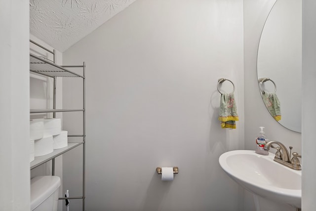 bathroom with a textured ceiling, toilet, and a sink