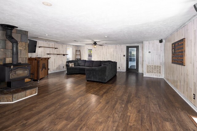 living room with a textured ceiling, dark hardwood / wood-style floors, a wood stove, and ceiling fan