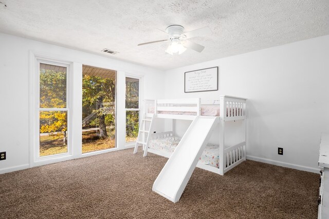 unfurnished bedroom with ceiling fan, dark carpet, and a textured ceiling