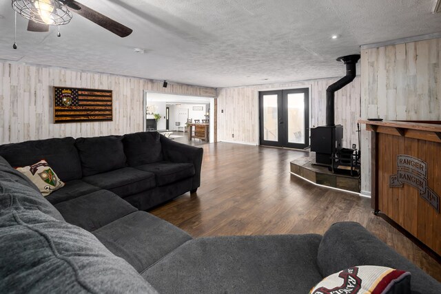 living room with wood walls, a wood stove, ceiling fan, a textured ceiling, and dark hardwood / wood-style flooring