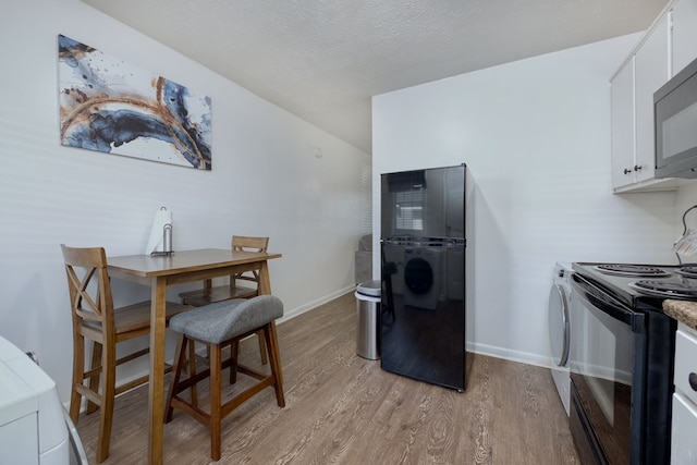 kitchen featuring washing machine and clothes dryer, a textured ceiling, white cabinets, light hardwood / wood-style floors, and black appliances