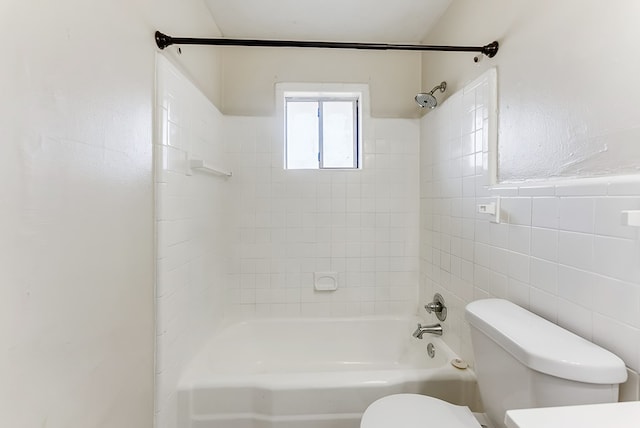 bathroom with tile walls, tiled shower / bath, and toilet