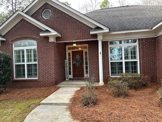 view of exterior entry with a shingled roof and brick siding