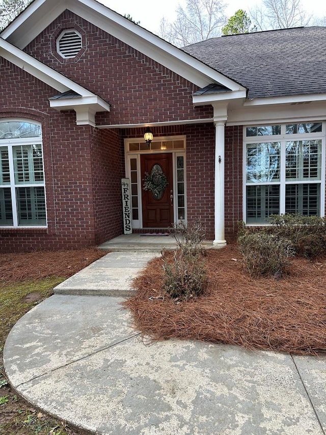 view of exterior entry featuring brick siding and a shingled roof