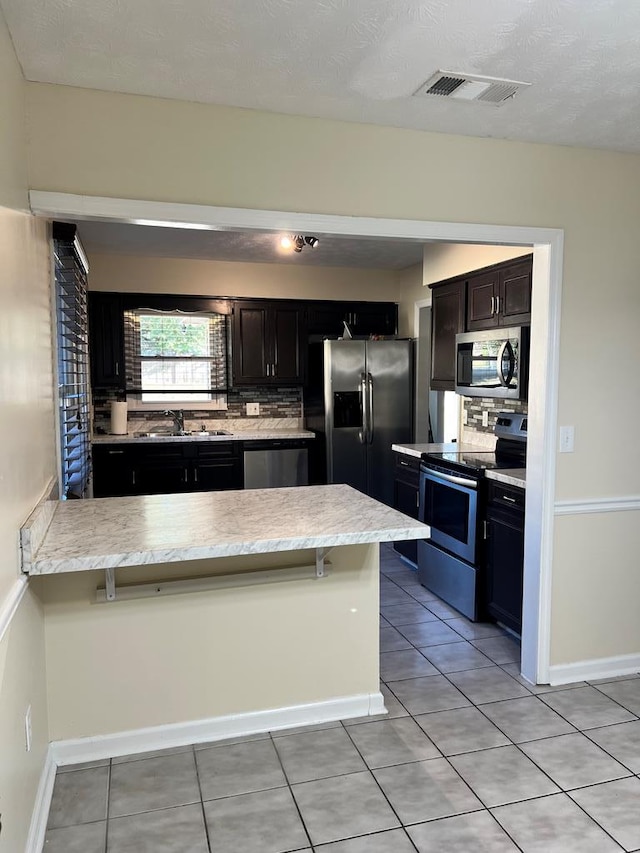 kitchen with stainless steel appliances, tasteful backsplash, a textured ceiling, a breakfast bar, and light tile patterned floors