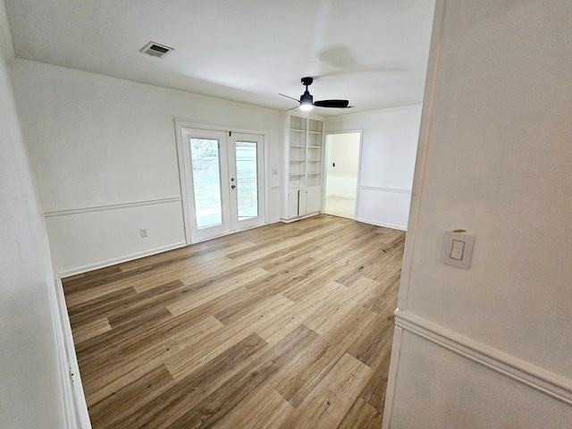 unfurnished room featuring built in shelves, ceiling fan, french doors, and light hardwood / wood-style floors