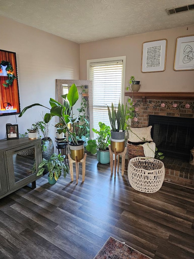 living area featuring dark wood-style floors, a textured ceiling, a brick fireplace, and visible vents