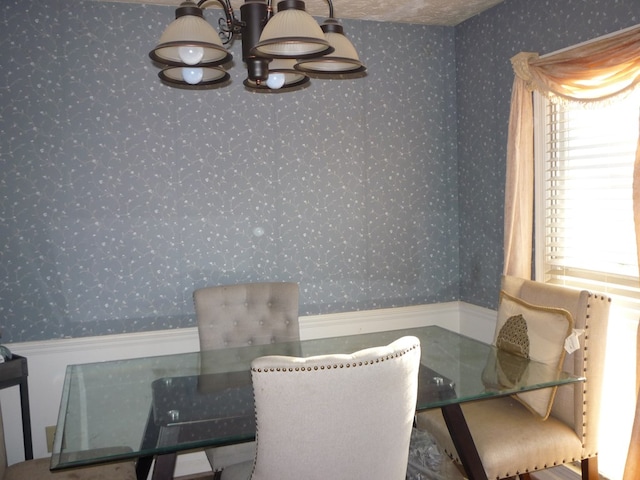 dining space with a wainscoted wall, an inviting chandelier, and wallpapered walls