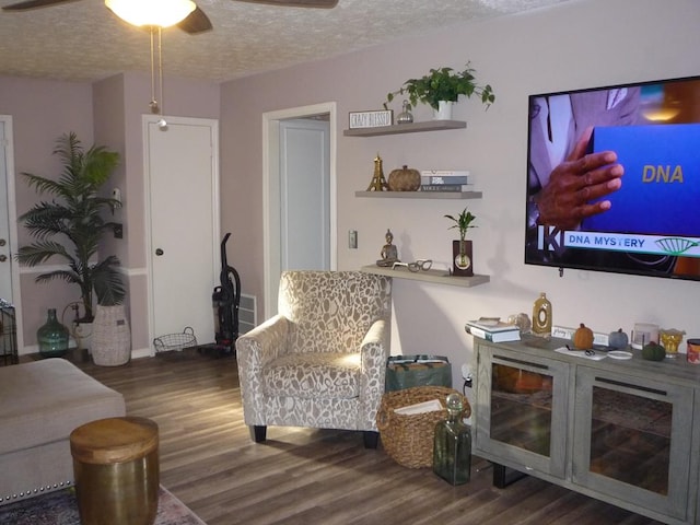 living area featuring ceiling fan, dark wood-style flooring, and a textured ceiling