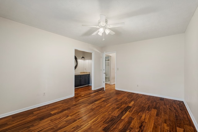 unfurnished bedroom with dark wood-style floors, connected bathroom, baseboards, and ceiling fan