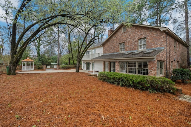 rear view of house with brick siding, concrete driveway, a gazebo, a balcony, and an attached garage