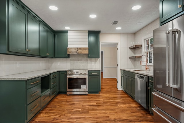 kitchen featuring green cabinetry, stainless steel appliances, wood finished floors, and a sink