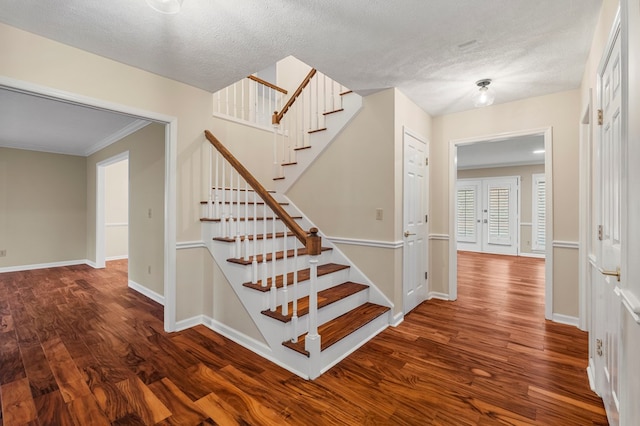 staircase featuring french doors, a textured ceiling, baseboards, and wood finished floors