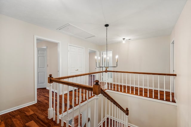 stairway with attic access, wood finished floors, baseboards, and a chandelier