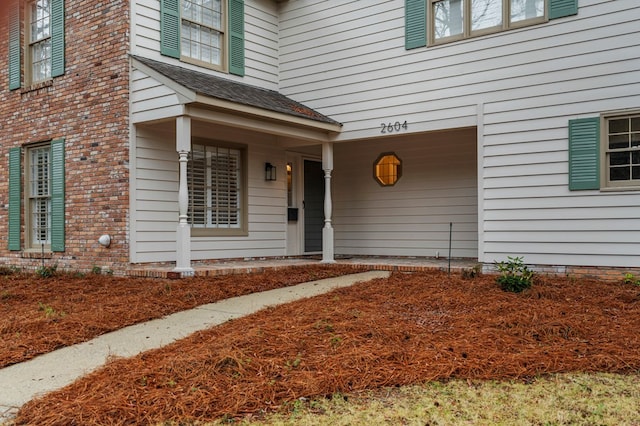 doorway to property with a porch and roof with shingles