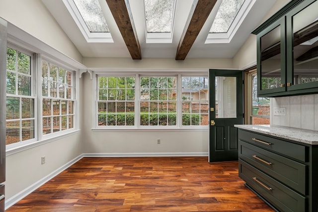 interior space featuring vaulted ceiling with skylight, baseboards, dark wood-style flooring, and green cabinetry