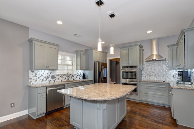 kitchen with appliances with stainless steel finishes, pendant lighting, gray cabinetry, a center island, and wall chimney range hood