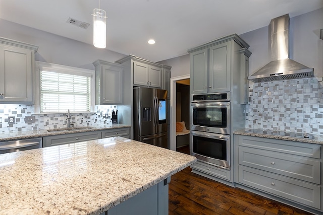 kitchen featuring wall chimney range hood, sink, appliances with stainless steel finishes, gray cabinetry, and hanging light fixtures